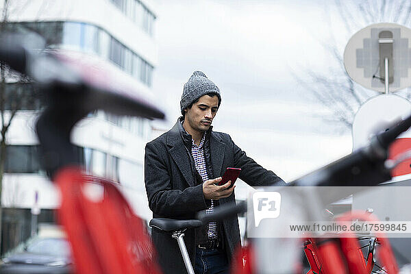 Man using smart phone for renting bicycle at parking station