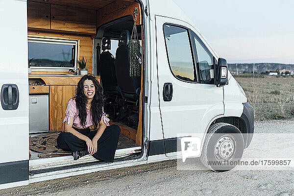 Glückliche junge Frau sitzt in einem Lieferwagen  der auf einer unbefestigten Straße geparkt ist