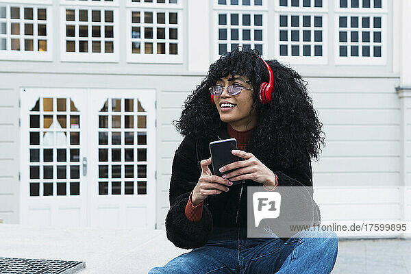 Fashionable young woman sitting with smart phone in front of building