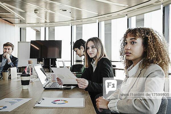 Young businesswomen with colleagues sitting at conference table in board room