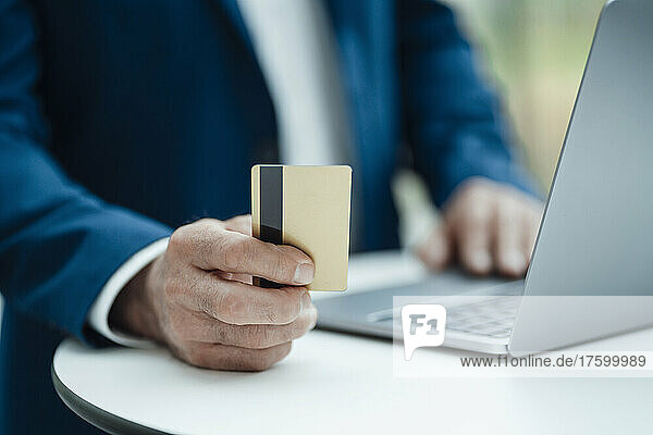 Hand of businessman holding credit card using laptop on table at office