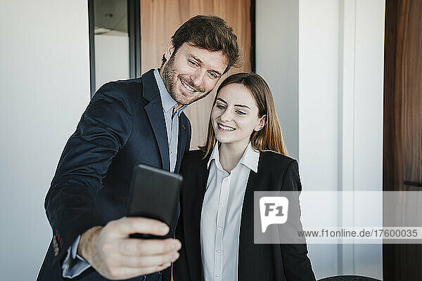 Lächelnder Geschäftsmann  der mit seinem Kollegen im Büro ein Selfie per Smartphone macht