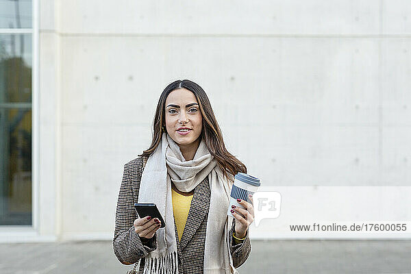 Junge Frau mit Smartphone und wiederverwendbarer Kaffeetasse auf Fußweg