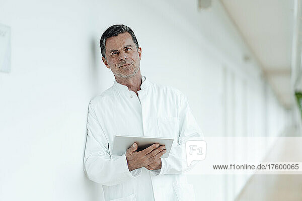 Scientist with tablet PC leaning on wall at medical clinic