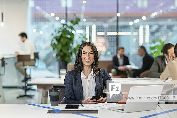 Lächelnde Geschäftsfrau mit Mobiltelefon im Büro