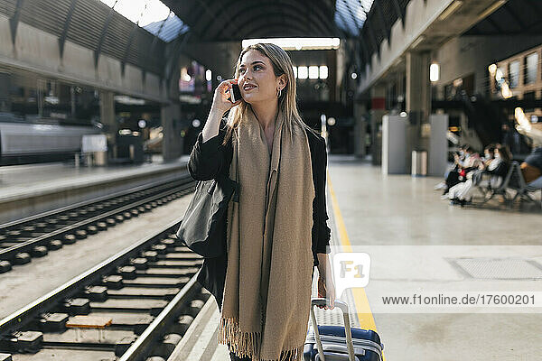 Woman with wheeled luggage talking on mobile phone at platform