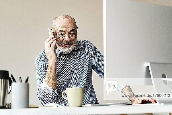 Senior freelancer talking on smart phone at desk