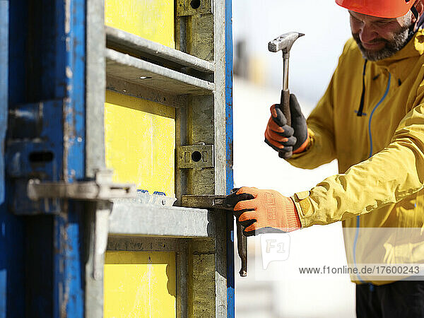 Worker hammering nail on formwork wall at construction site