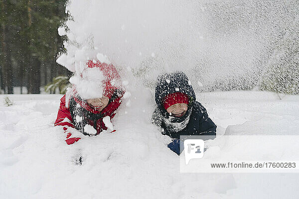 Playful twin brothers throwing snow on each other in forest