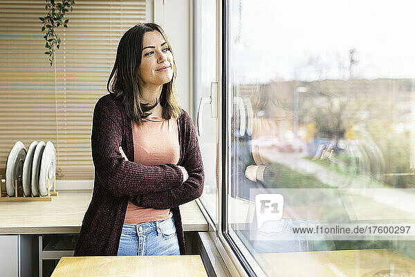 Young woman with arms crossed looking out of window at home