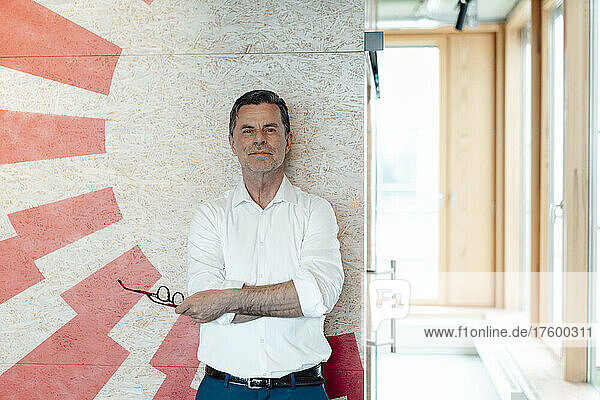 Businessman holding eyeglasses standing in front of patterned wall at office