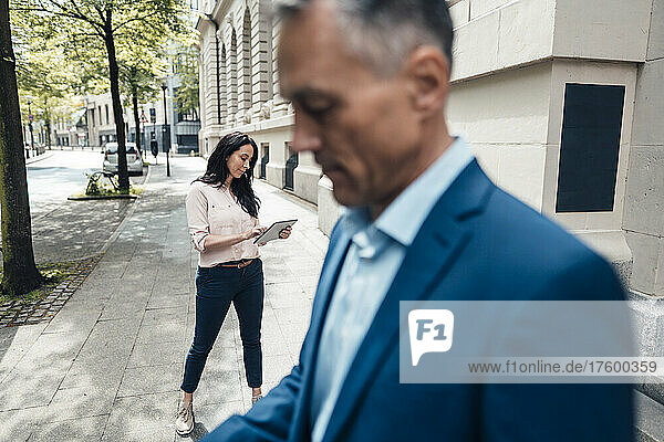 Businesswoman using tablet PC with mature businessman in foreground
