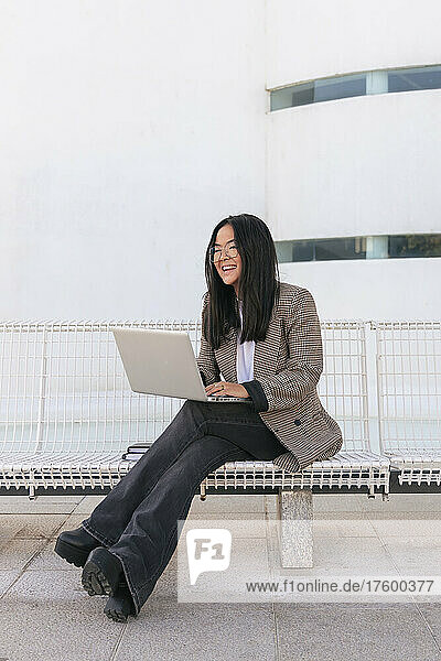 Smiling businesswoman with laptop sitting on bench