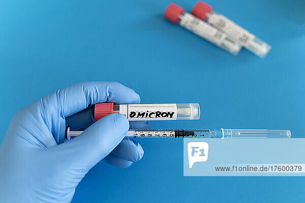 Medical expert holding swab tube and syringe on blue background