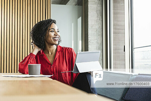 Smiling businesswoman with tablet PC looking through window at work place