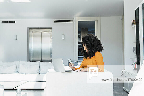 Woman using mobile phone by laptop in living room