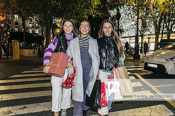 Smiling friends walking with shopping bags on road in city