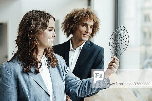Smiling businesswoman with businessman looking at leaf model in office