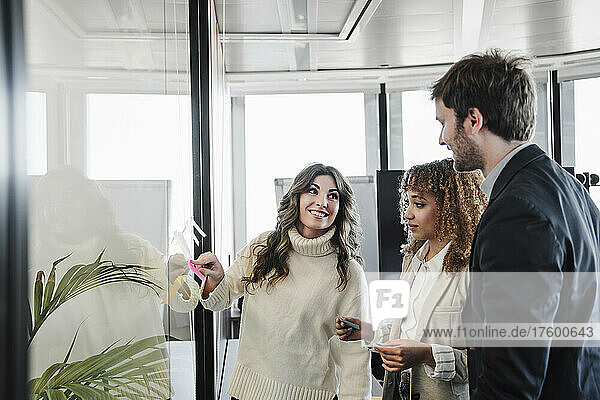 Smiling businesswoman explaining adhesive notes to colleagues in office
