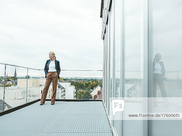Nachdenkliche Geschäftsfrau steht vor klarem Himmel auf dem Bürobalkon