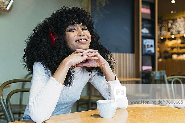 Smiling young woman with clasped hands on chin listening music at cafe