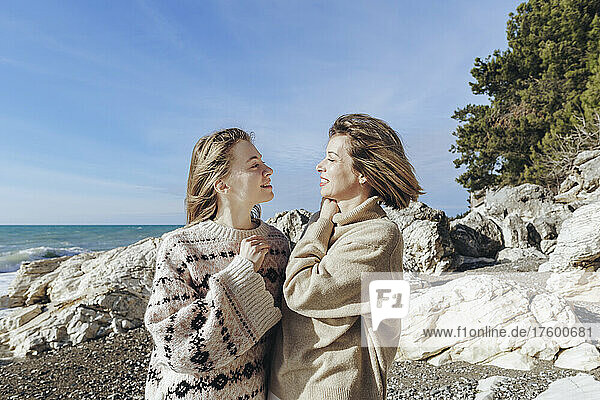Woman with daughter wearing sweater at beach on sunny day