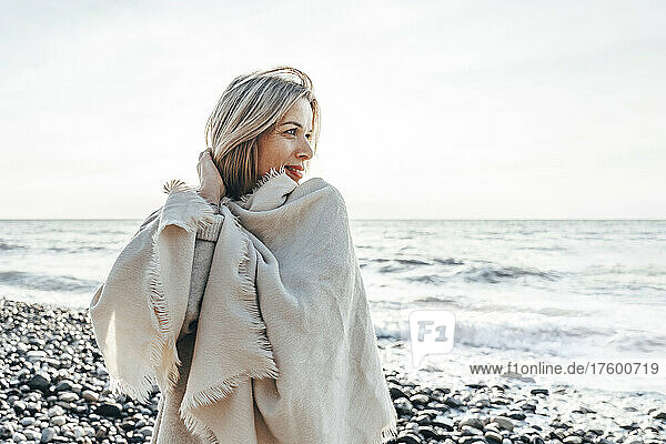 Smiling blond woman wrapped in blanket at beach