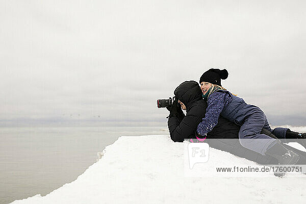 Smiling girl lying on mother photographing through camera in winter