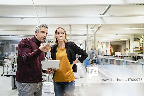 Businessman with tablet PC discussing ideas with blond colleague in factory