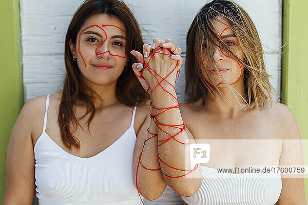 Young women with thread holding hands in front of wall