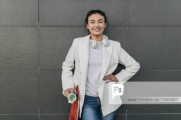 Smiling woman with skateboard and headphones in front of wall