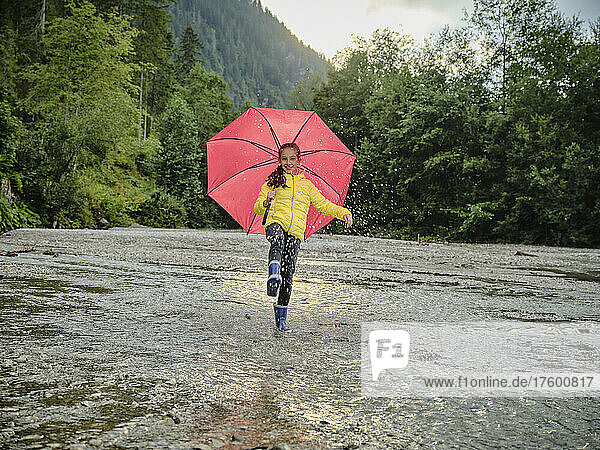 Happy girl holding umbrella and splashing water in lake
