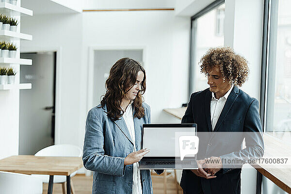 Young businesswoman discussing with businessman over laptop at coworking office