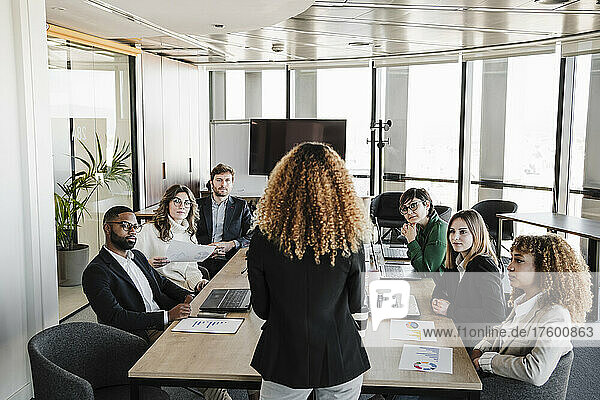 Businesswomen and businessmen listening to colleague discussing strategy in board room
