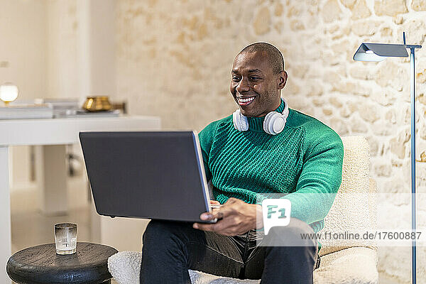 Glücklicher Mann mit kabellosen Kopfhörern und Laptop  der zu Hause arbeitet