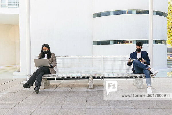 Business colleagues following social distancing sitting on bench