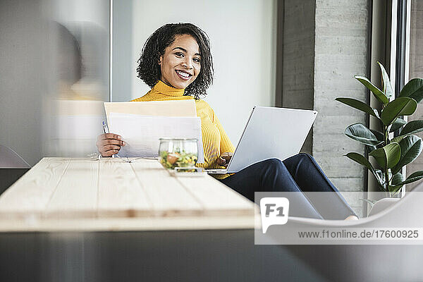 Smiling businesswoman holding documents in office