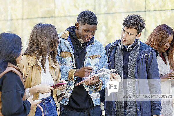 Multiracial friends discussing over book on campus