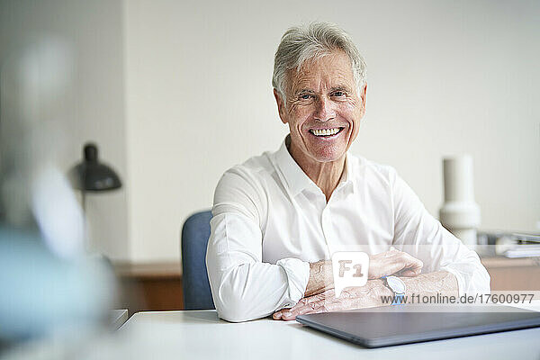 Happy senior businessman with laptop at desk in studio