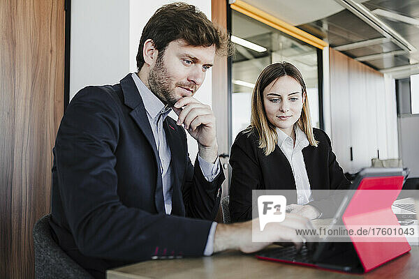 Businessman sharing tablet PC with businesswoman sitting at desk in office