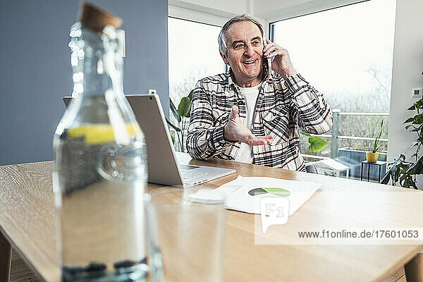 Smiling senior man talking on smart phone sitting at table