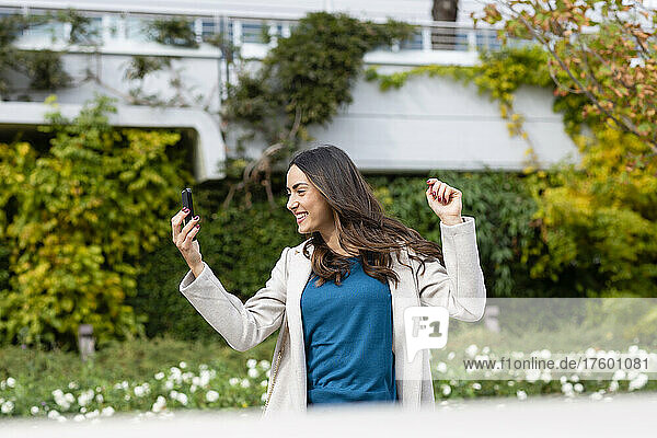 Carefree woman with smart phone dancing in city