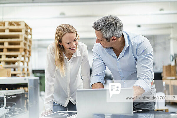 Smiling businessman and businesswoman discussing over laptop in industry