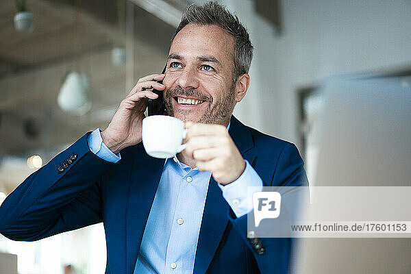 Smiling businessman holding coffee cup talking on mobile phone