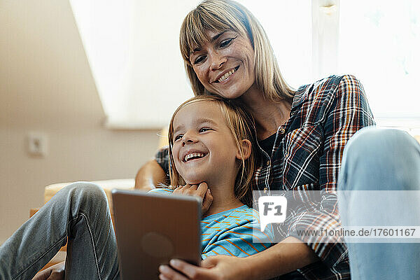 Son laughing by mother using tablet PC at home