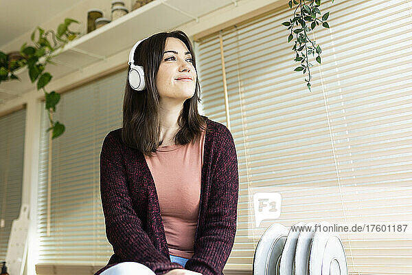 Smiling woman listening music on headphones in kitchen at home