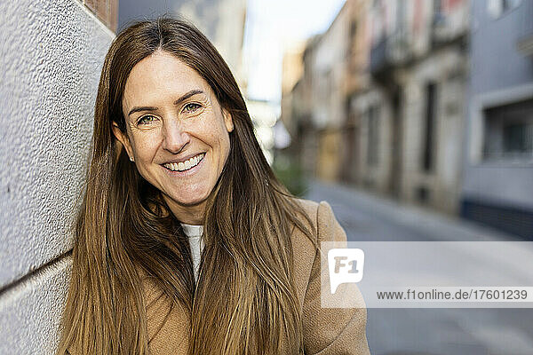 Happy woman with brown hair leaning on wall