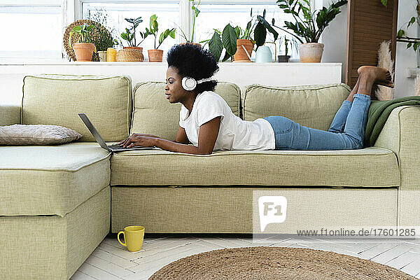 Young businesswoman with headphones using laptop on sofa at home