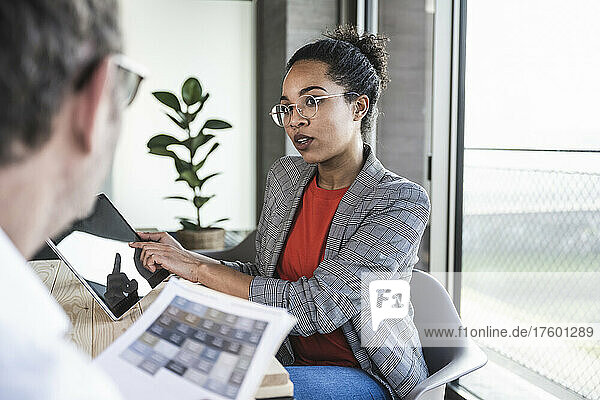 Businesswoman discussing over tablet computer with colleague at work place