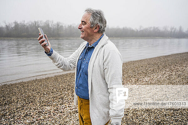 Smiling senior man doing video call through mobile phone at beach